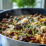 Steaming skillet of Comforting Ground Beef Orzo Dinner served with bell peppers and peas in tomato broth.