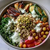 A close-up of creamy tahini dressing drizzled over steamed kale, chickpeas, and sweet peppers in a Mediterranean Buddha Bowl.