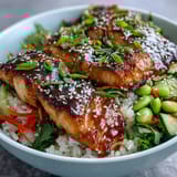 Flaky Asian-Inspired Salmon Bowl topped with sesame seeds, served on fluffy rice with crisp vegetables and a lime wedge.