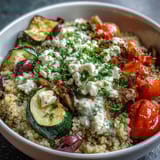 A close-up of a Mediterranean Buddha Bowl reveals Kalamata olives, juicy cherry tomatoes, and chopped parsley over a bed of quinoa, with a generous dollop of hummus and Greek yogurt.