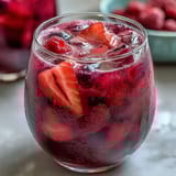 A vibrant glass of pink drink with strawberry açaí and coconut milk, garnished with fresh strawberry slices.