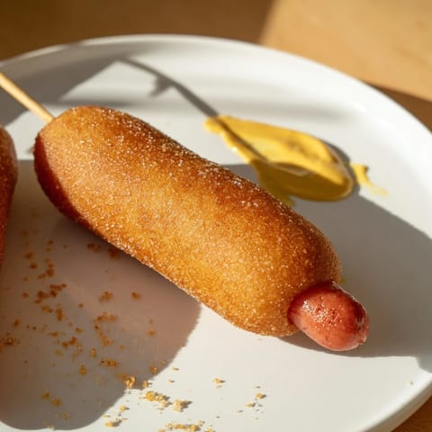 A close-up of a perfectly fried corn dog, with a sweet, savory cornmeal batter coating.