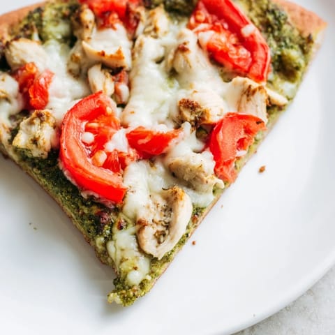 Golden-brown thin-crust Chicken Pesto Pizza topped with melted mozzarella, juicy tomato slices, and fresh basil leaves on a rustic wooden board.  