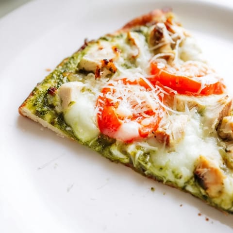 Freshly baked Chicken Pesto Pizza with vibrant green basil pesto, tender chicken pieces, and bubbling cheese served on a cutting board.  