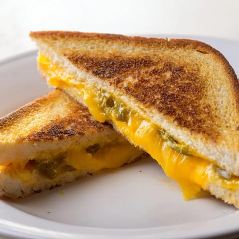 Spicy jalapeño popper grilled cheese sandwich, bubbling with cream cheese filling between crispy golden bread ready to serve.