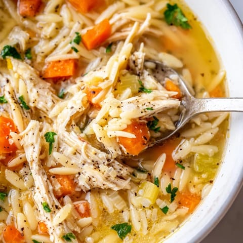 Lemon Pepper Chicken Orzo Soup in a white pot, featuring vibrant carrots, celery, and lemon wedges on the side for a zesty, comforting meal.