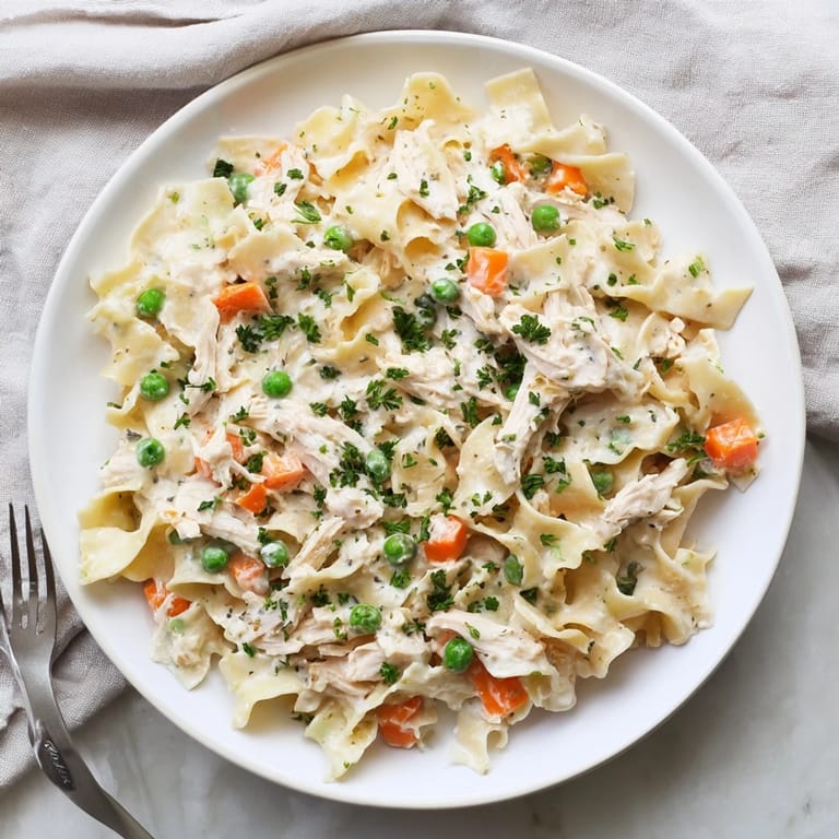 Steam rises from a colorful Spring Chicken Noodle Skillet, where juicy chicken, peas, and carrots mingle with silky noodles in a light cream sauce, perfect for a weeknight family dinner.