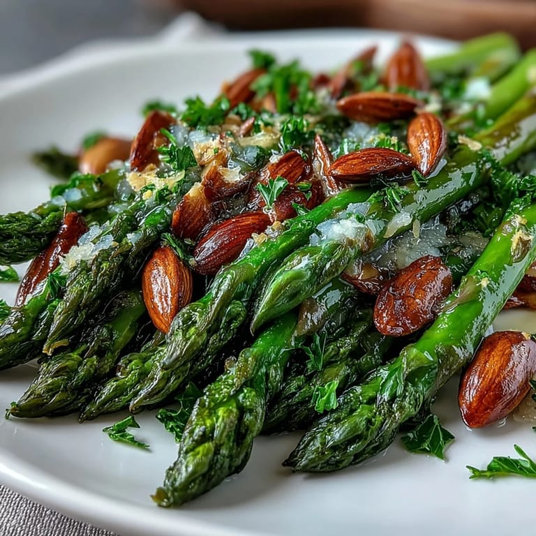 Asparagus spears sautéed in lemon butter, topped with golden toasted almonds, served on a white platter for an elegant, easy spring side dish.