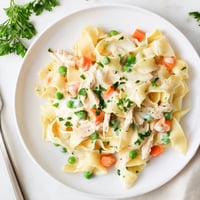 Golden egg noodles, tender shredded chicken, sweet peas, and carrots swim in a creamy, thyme-scented sauce in this cozy Spring Chicken Noodle Skillet, ready to serve.