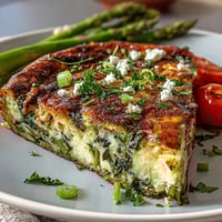 Healthy Easy Spring Veggie Frittata with fresh asparagus, spinach, and cherry tomatoes, baked golden and topped with herbs and feta.