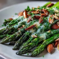 Lemon Butter Asparagus with Almonds in a white serving bowl, garnished with toasted almonds and fresh parsley, showcasing vibrant green asparagus spears in a buttery lemon sauce.